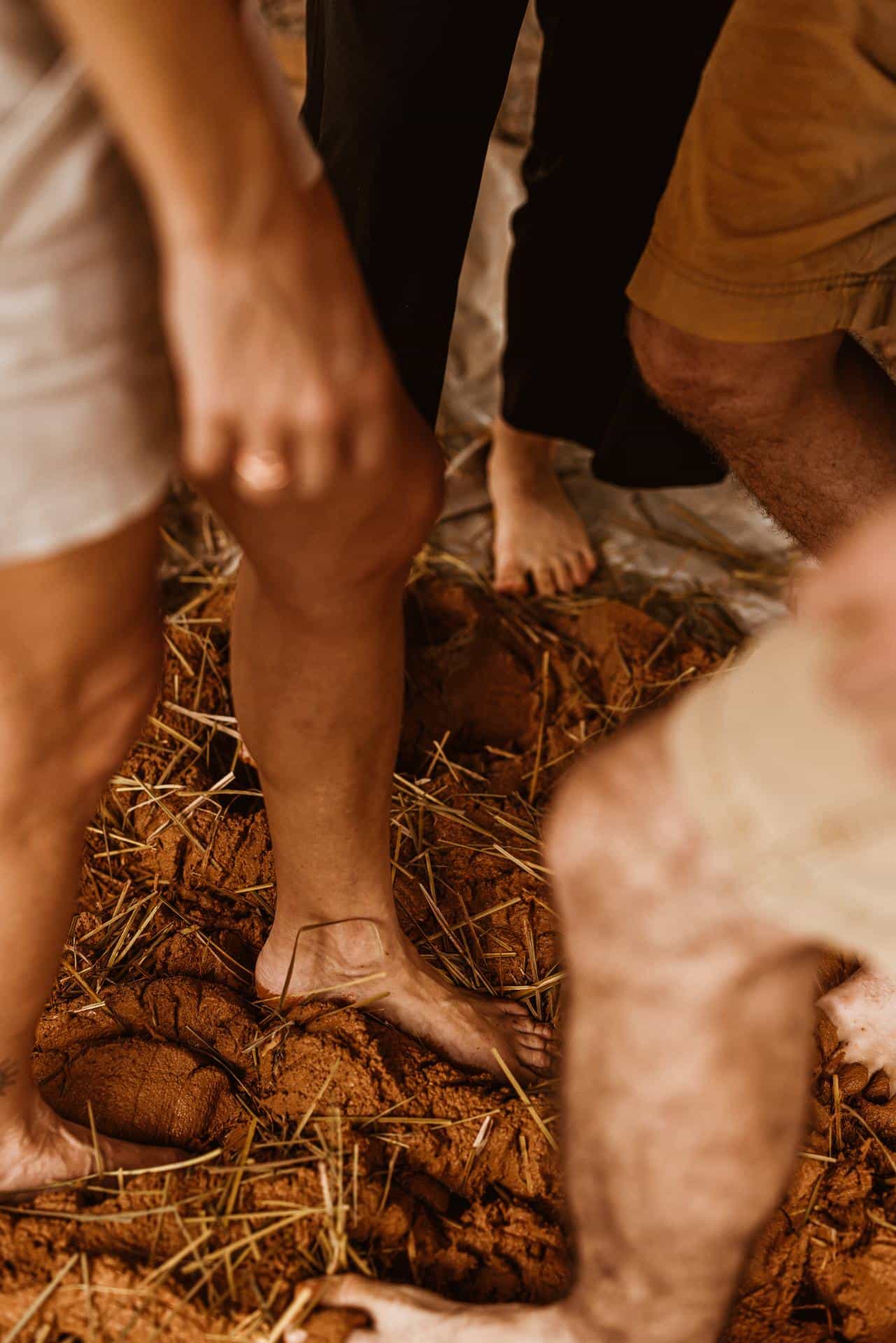 Bare feet working wet clay and straw during a family building day at the homestead