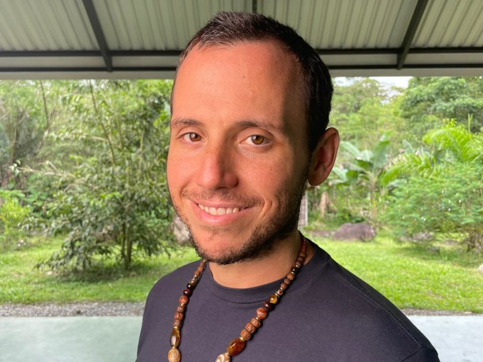 Michael standing outdoors at the homestead, wearing a beaded necklace